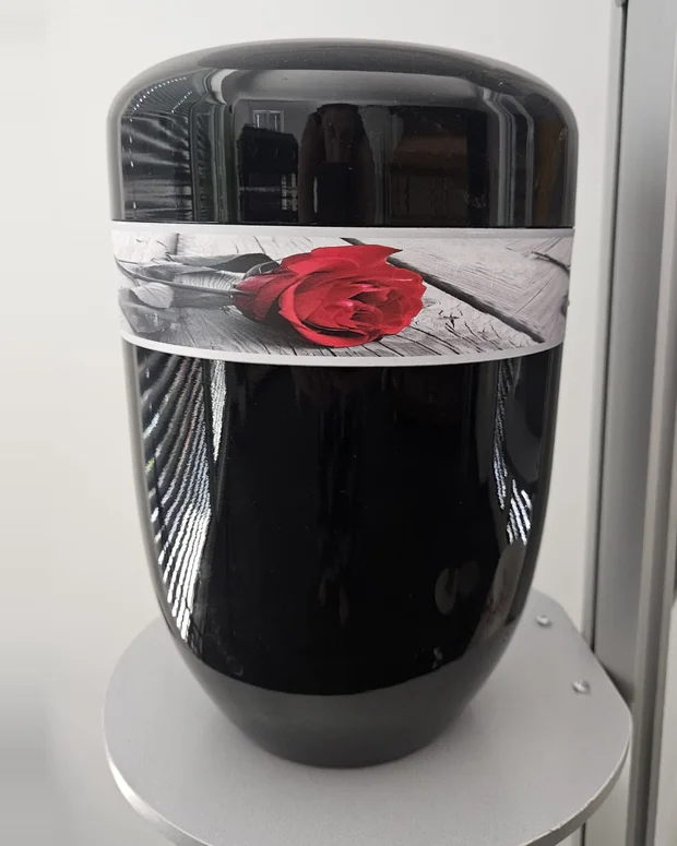 Schwarze Urne mit hohem Glanz, umlaufendes Band mit einer roten Rose