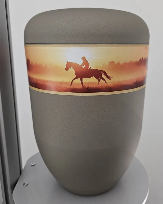 Graue Urne mit einem Band: ein Reiter zu Pferd im Abendlicht